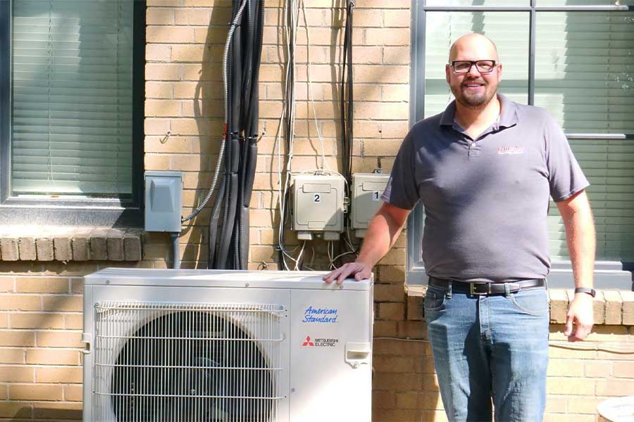 Technician standing next to an American Standard outdoor HVAC unit.