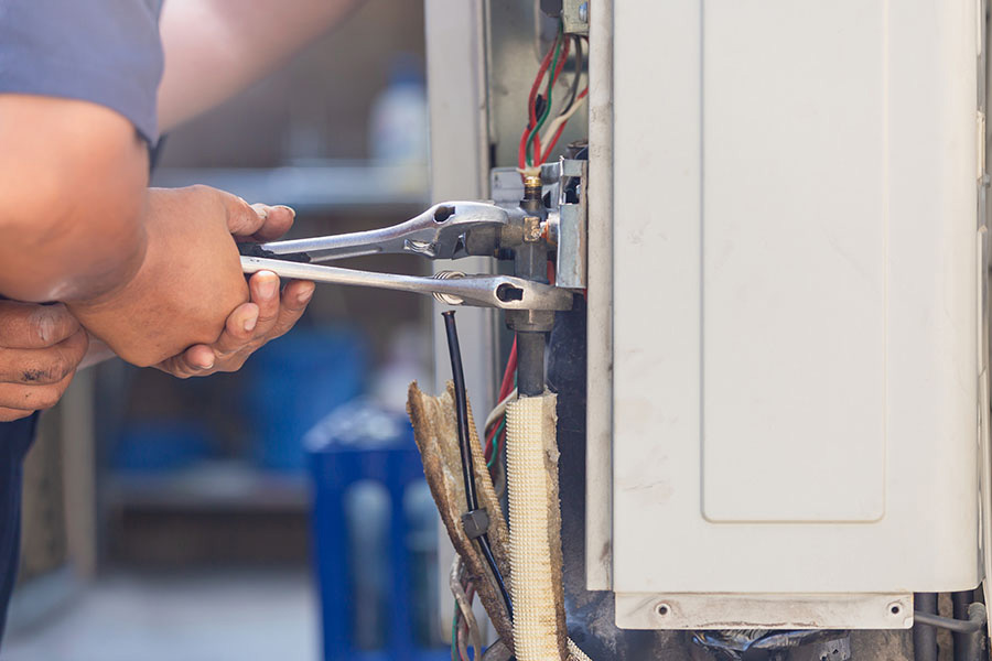 HVAC technician tightening refrigerant connections inside an outdoor unit while repairing common ac problems