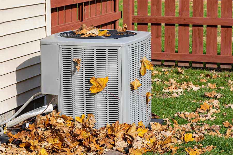 Outdoor ac unit covered with fallen leaves beside a home