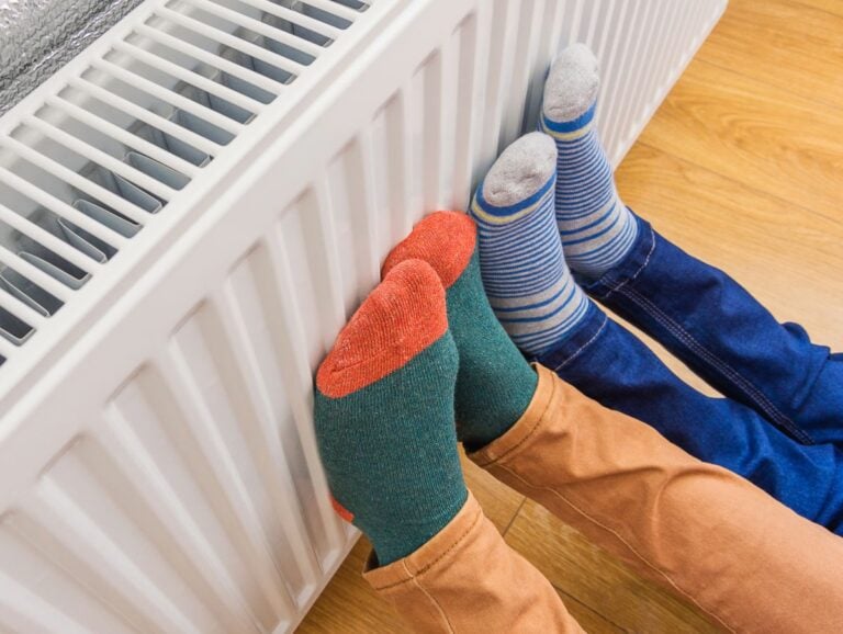 Woman and child wearing colorful pair of woolly socks warming cold feet in front of heating radiator