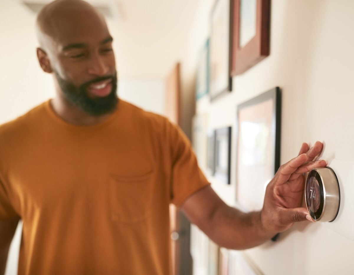 Man Adjusting Digital Central Heating Thermostat At Home