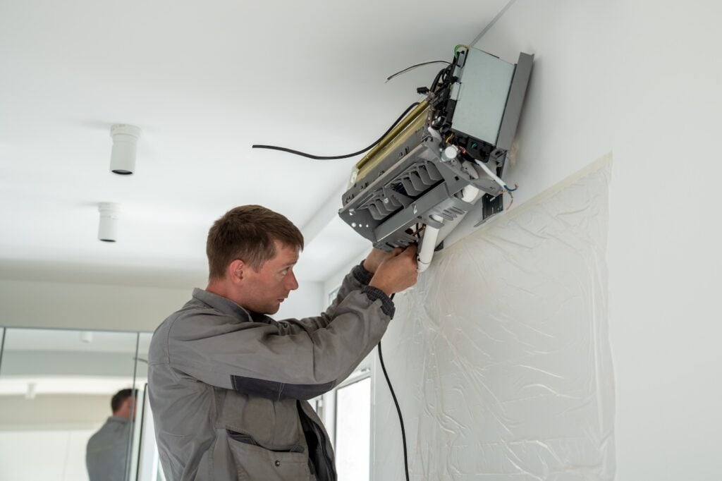 Man technician worker in uniform fixing repairing apartment air conditioner, installing wall-mounted mini split