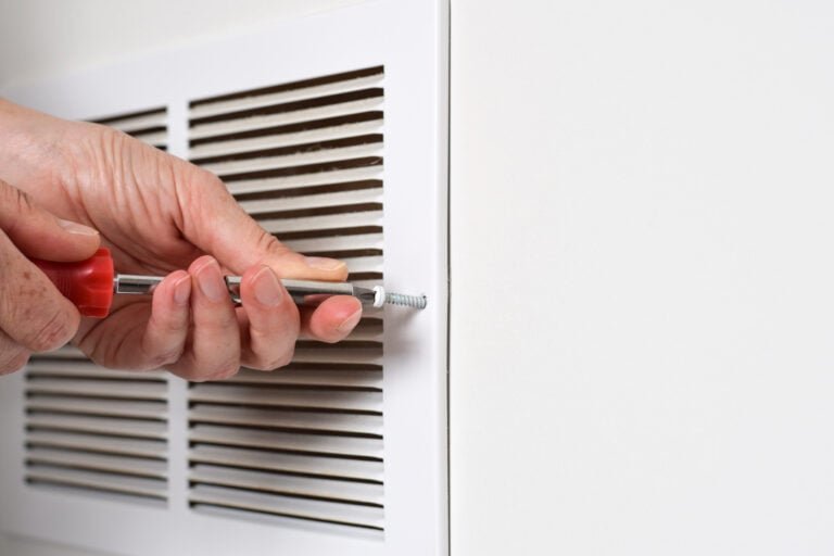 Person's hand using screwdriver to open return air vent for cleaning